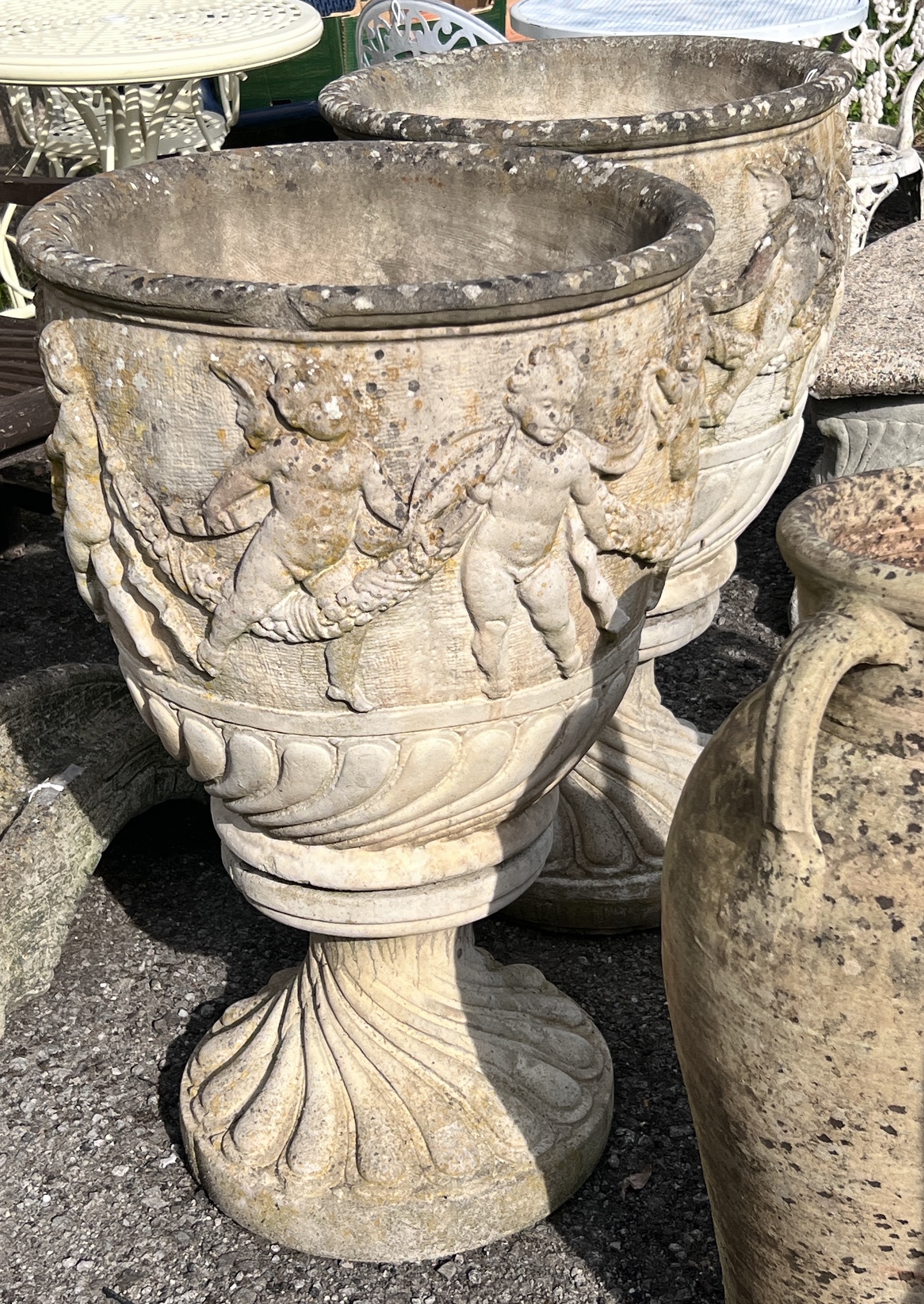 A pair of large circular reconstituted stone garden planters, moulded with a band of putti on square bases, diameter 53cm, height 89cm